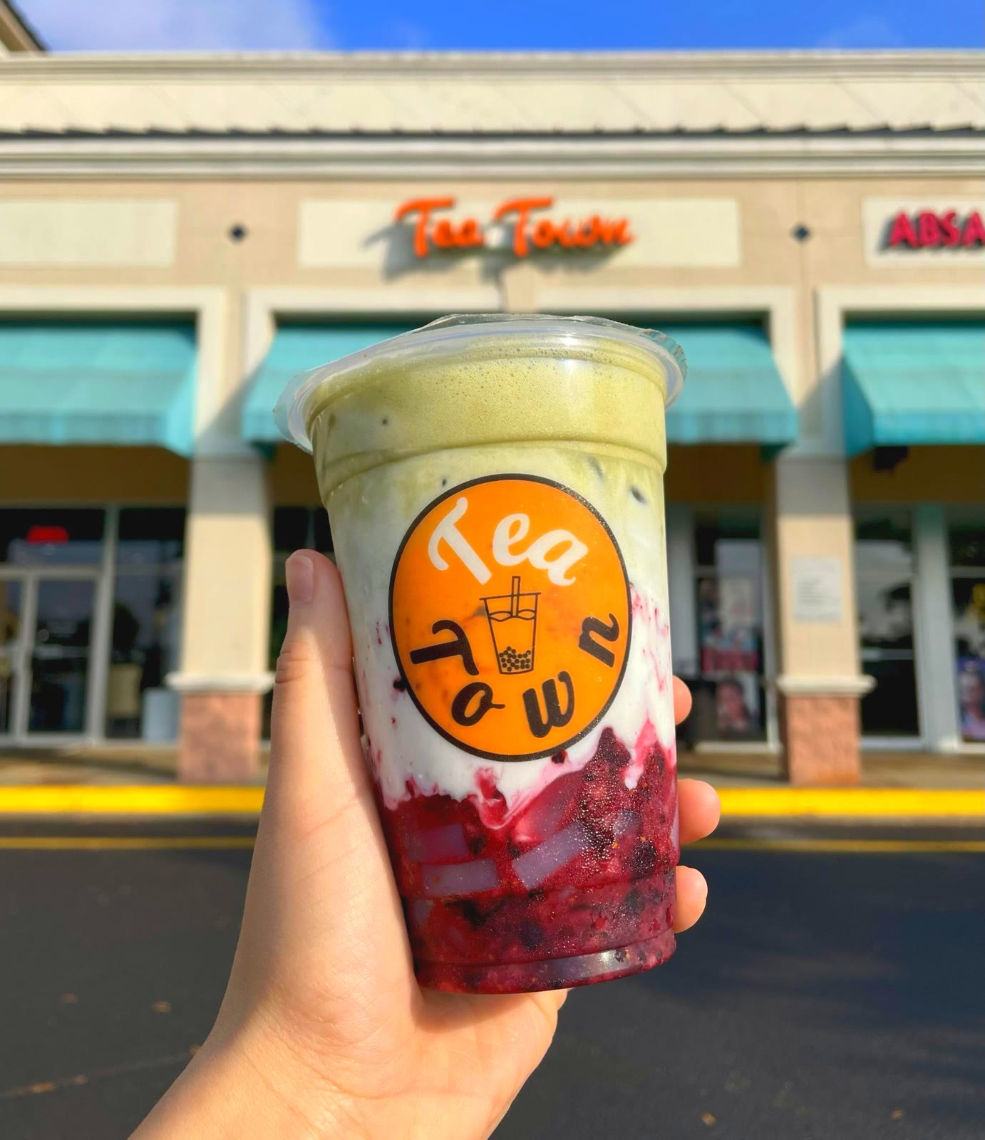 A layered fresh fruit boba drink held up in front of the Tea Town storefront
